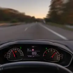Widok z perspektywy kierowcy. Na desce rozdzielczej widać prędkościomierz wskazujący 89 km/h. To właśnie co robimy podczas jazdy samochodem.