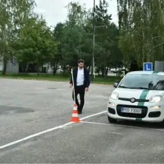 Młody mężczyzna ustawia pachołek na placu manewrowym, przygotowując się do egzaminu praktycznego.