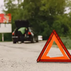 Trójkąt ostrzegawczy na drodze, obok samochodu z otwartym bagażnikiem. Awaria samochodu w terenie zabudowanym.