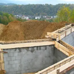 Budowa fundamentów zbrojonych, przygotowana zgodnie z pozwoleniem na budowę. W tle widać kopce ziemi i zabudowania.