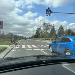 Niebezpieczne wyprzedzanie na pasach na drodze dwupasmowej. Niebieski SUV omija rowerzystkę stojącą przy przejściu.