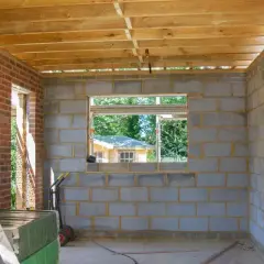 Budynek gospodarczy w budowie, z bloczków betonowych i cegły, z widocznym stropem drewnianym. Zgodnie z prawem budowlanym, to obiekt pomocniczy.
