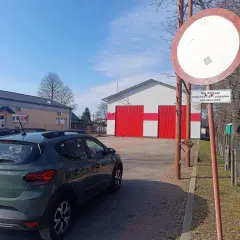 Zielony Dacia Sandero zaparkowany przy remizie OSP. Znak zakazu wjazdu, który nie dotyczy pojazdów OSP, może sugerować mandat za wjazd pod zakaz.
