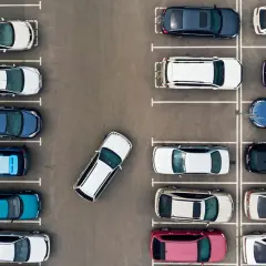 Widok z góry na parking, gdzie samochody zaparkowane są prostopadle. Widać różne kolory i modele aut.