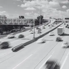 Rozmyte samochody pędzą po wielopasmowej autostradzie. Widoczny znak drogowy i wiadukt. Specustawa drogowa w akcji.
