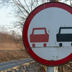 Znak drogowy informujący o końcu zakazu wyprzedzania. Dwa samochody, czerwony i czarny, symbolizują koniec ograniczenia.