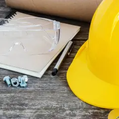 Żółty kask, okulary ochronne, śruby i notatnik leżą na drewnianym stole. Kto przechowuje dziennik budowy po zakończeniu budowy?
