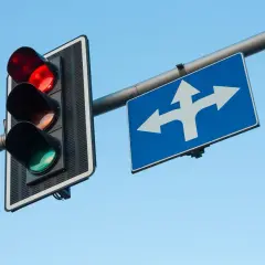 Czerwone światło na sygnalizatorze i znak wskazujący kierunki jazdy. Pamiętaj, co grozi za przejazd na czerwonym świetle – mandat i punkty karne.