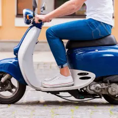 Młody człowiek w jeansach i białej koszulce, który jeszcze nie ma prawa jazdy, jedzie skuterem.