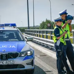 Policjanci kontrolują prędkość na drodze. Obok radiowóz z włączonymi sygnałami. Bezpieczne prowadzenie pojazdu to priorytet.