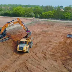 Koparka i wywrotka pracują na placu budowy, niwelując teren. W tle spychacz. Kary za niwelację terenu mogą być wysokie.