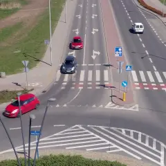 Samochody poruszają się po skrzyżowaniu z oznakowaniem sugerującym rondo turbinowe.
