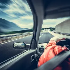 Kierowca w pomarańczowej kurtce jedzie autostradą. Widać rozmycie drogi i krajobrazu, co sugeruje dużą prędkość. Wymaga to ostrożności, a nawet szczególnej ostrożności.