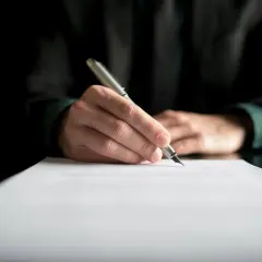 Dłoń pisze piórem na dokumencie. Może to być dziennik budowy, przerwa we wpisach lub ważny kontrakt.