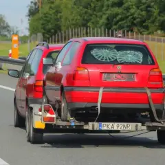 Czerwony Volkswagen Golf na lawecie, holowany przez inny samochód. To dowód, że automatem można holować inne auto, choć nie jest to standardowa sytuacja.