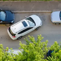 Biały SUV wykonuje parkowanie równoległe przodem między czarnym SUV-em a srebrnym sedanem.