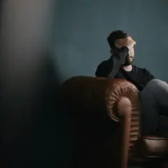 Mężczyzna siedzi na kanapie, zasłaniając twarz ręką. Wygląda na przygnębionego po negatywnym egzaminie na prawo jazdy.