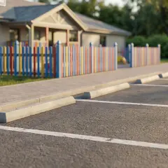 Parking spaces viewed from a 45-degree angle, with a colorful fence and building in the background.