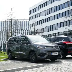 Szary i czarny samochód zaparkowane obok siebie. Znak "Płatny" informuje o rodzajach parkowania.
