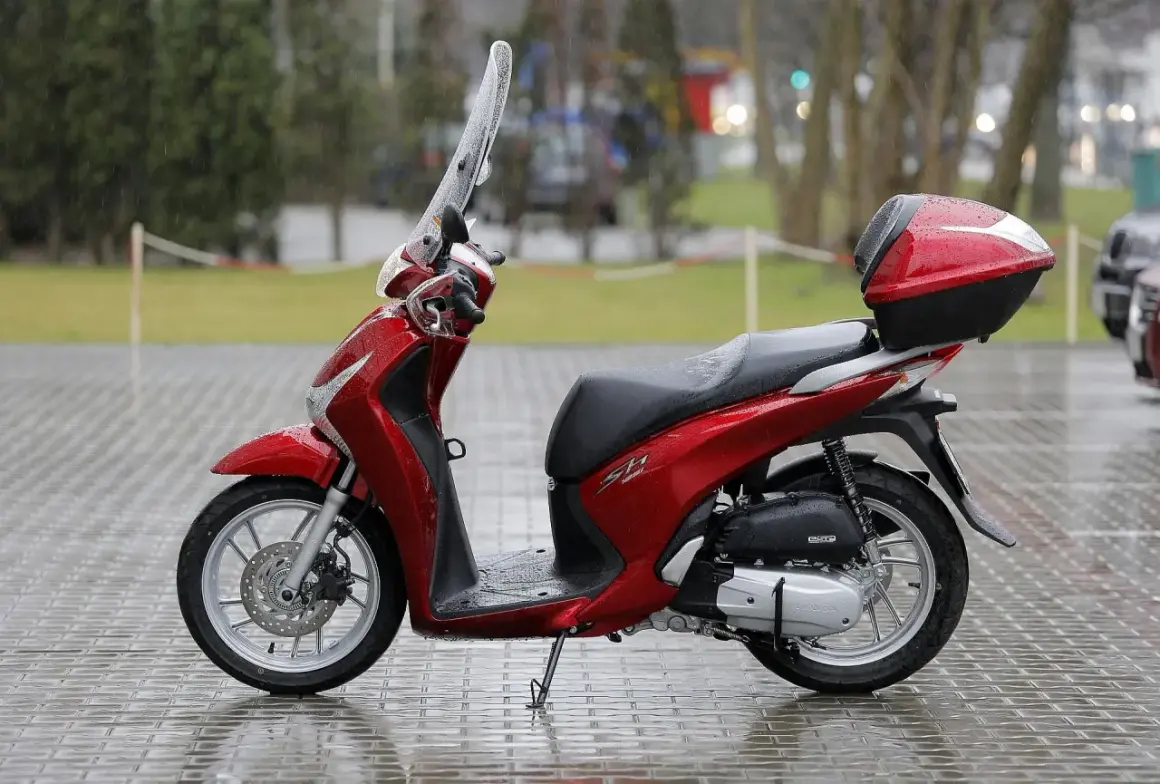 Czerwony skuter Honda SH z kufrem, gotowy do jazdy. W Polsce od ilu lat można jeździć skuterem? Od 14 lat na 50cc, od 18 lat na większe pojemności.