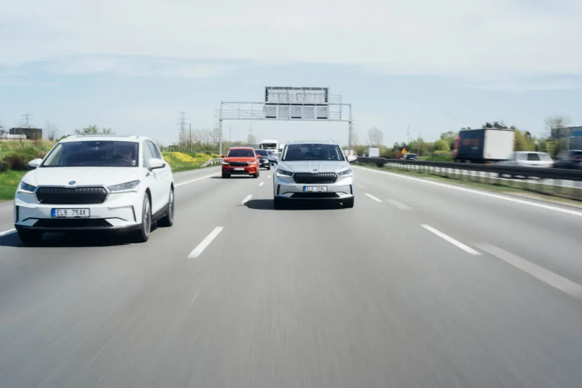 Na autostradzie biały i srebrny SUV jadą z zachowaniem bezpiecznej odległości między samochodami na światłach.