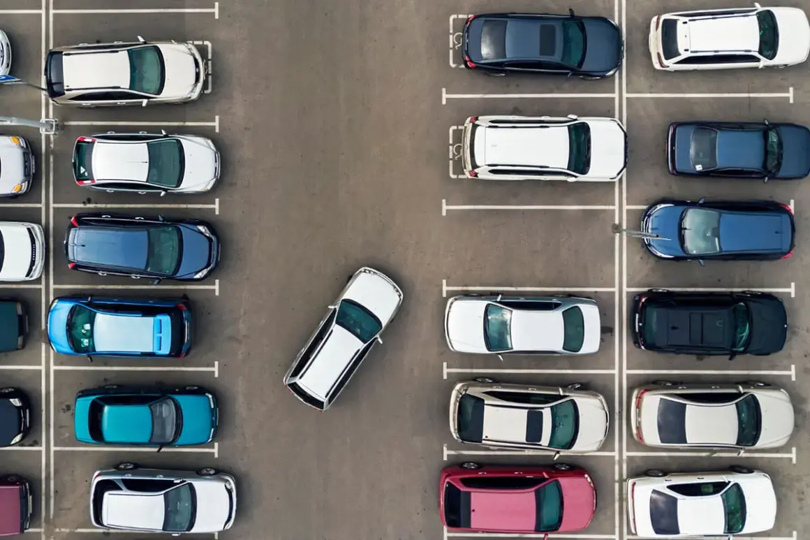 Widok z góry na parking, gdzie samochody zaparkowane są prostopadle. Widać różne kolory i modele aut.