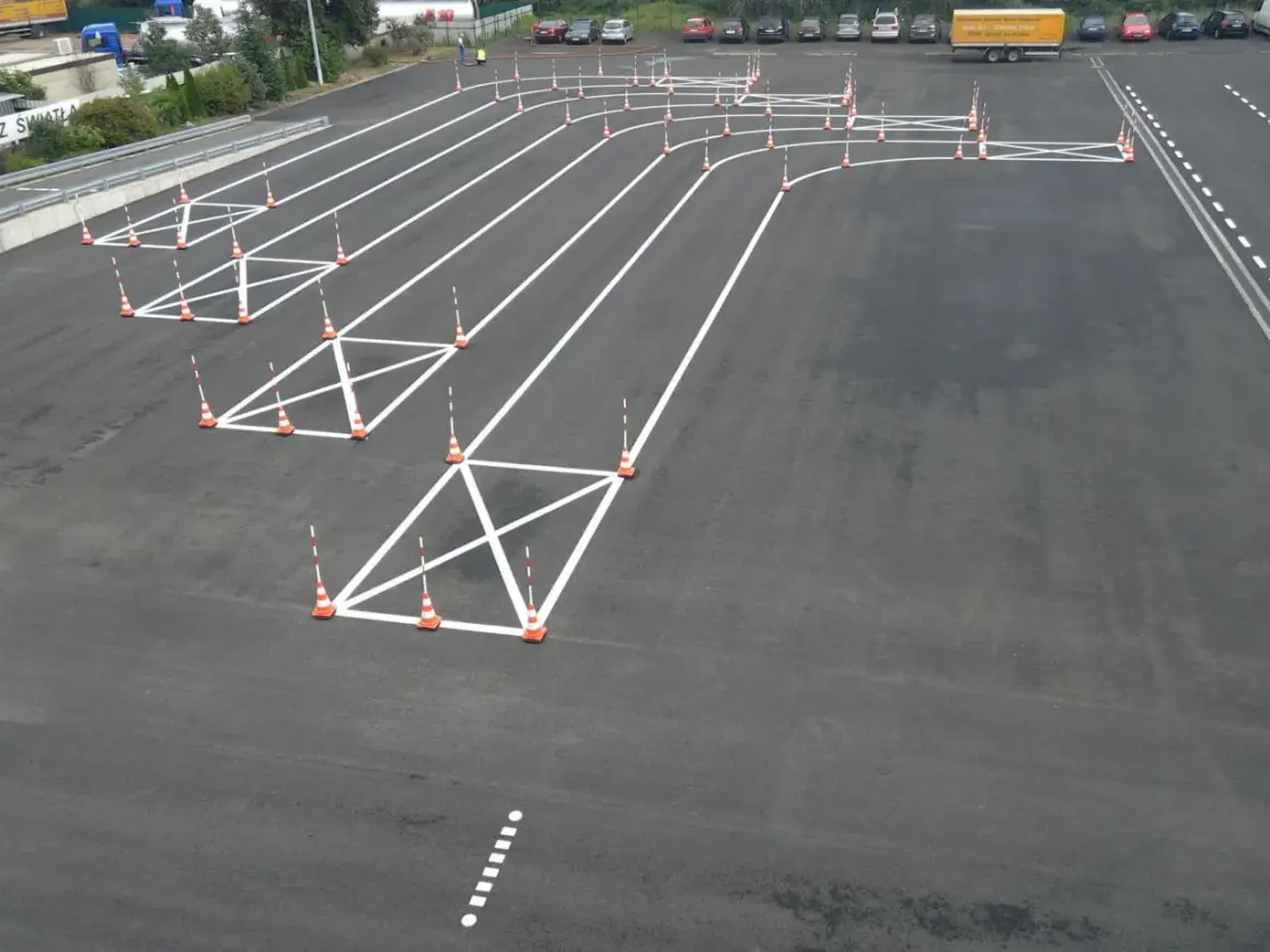 Plac manewrowy z pachołkami i białymi liniami, idealny do nauki, jak kręcić kierownicą podczas jazdy po łuku.