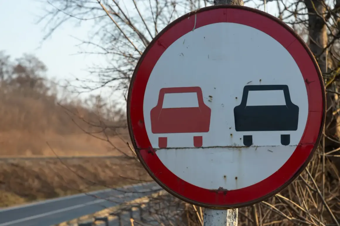 Znak drogowy informujący o końcu zakazu wyprzedzania. Dwa samochody, czerwony i czarny, symbolizują koniec ograniczenia.