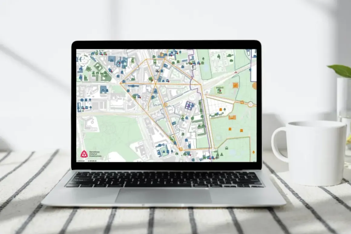 Mapa na ekranie laptopa pokazuje obszar wpisany do rejestru zabytków, z zaznaczonymi budynkami i ulicami.