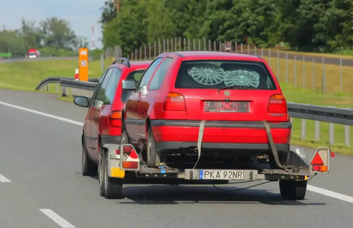 Czerwony Volkswagen Golf na lawecie, holowany przez inny samochód. To dowód, że automatem można holować inne auto, choć nie jest to standardowa sytuacja.