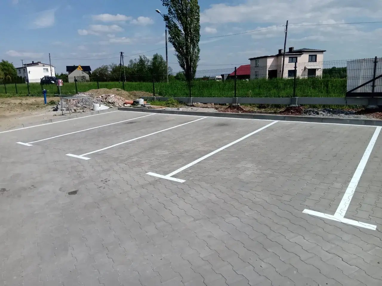 Świeżo wyznaczone miejsca parkingowe, idealne do parkowanie prostopadłe. W tle domy i zielona trawa.