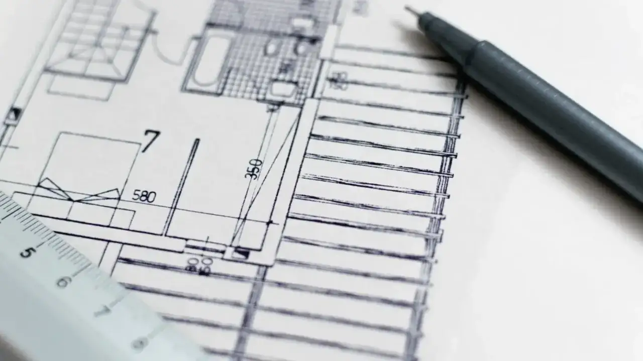 Plan architektoniczny z linijką i długopisem. Precyzja jest kluczowa, by uniknąć odpowiedzialności projektanta za błędy w projekcie.
