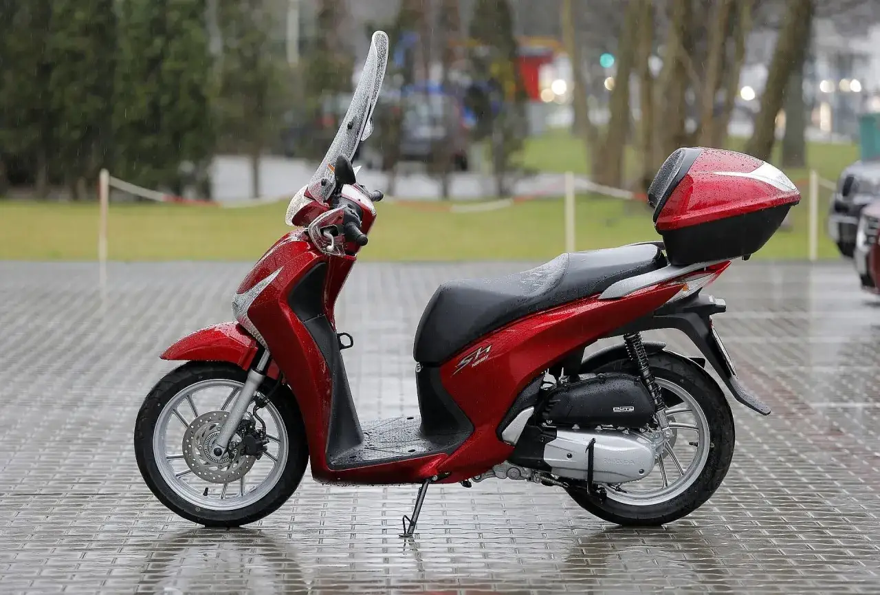 Czerwony skuter Honda SH z kufrem, gotowy do jazdy. W Polsce od ilu lat można jeździć skuterem? Od 14 roku życia na 50cc.