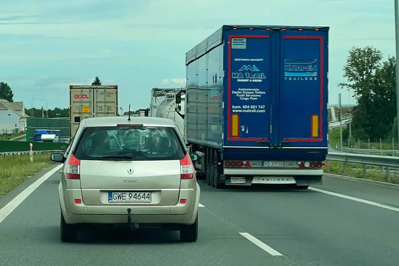 Na autostradzie widać ruch samochodów, w tym duży niebieski tir. Czy tiry mogą się wyprzedzać na autostradzie? To zależy od przepisów i sytuacji na drodze.