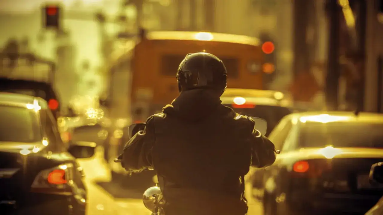 Motocyklista w korku, zastanawia się, jaka powinna być odległość między samochodami. Słońce przebija się przez mgłę, tworząc złoty blask.