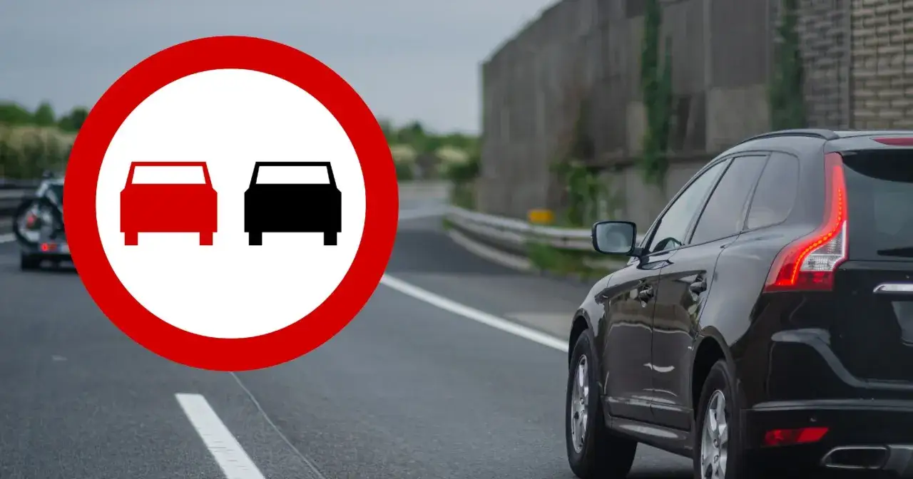 Znak zakazu wyprzedzania na drodze jednokierunkowej. Czarny SUV jedzie po drodze, a z lewej strony widać znak.