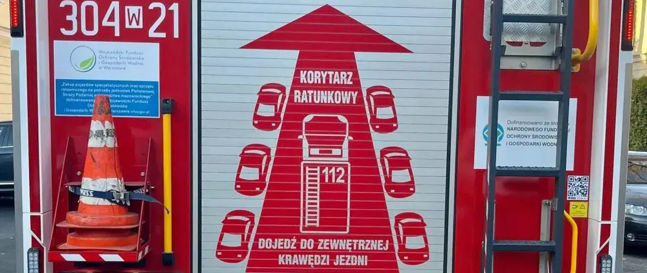Na drzwiach wozu strażackiego grafika symbolizująca korytarz życia, z samochodami i numerem 112.
