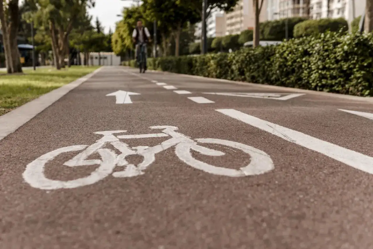 Wyraźny symbol roweru na ścieżce rowerowej, z białymi strzałkami kierunkowymi i rozmytą postacią cyklisty w tle.